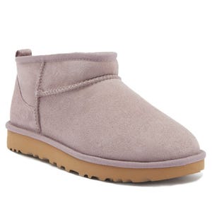 A suede ankle-height boot in a dusty pink color with a rounded toe, visible stitching, and a pull tab at the back, featuring a rubber sole with a tread pattern for grip.