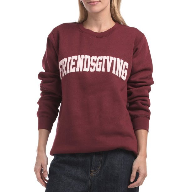 A woman wears a maroon sweatshirt featuring the word \“FRIENDSGIVING\“ in bold white letters on the front.