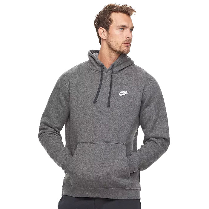A man is wearing a dark gray Nike hoodie with a white logo on the chest. He has his hands in the front pocket and is looking to the side.