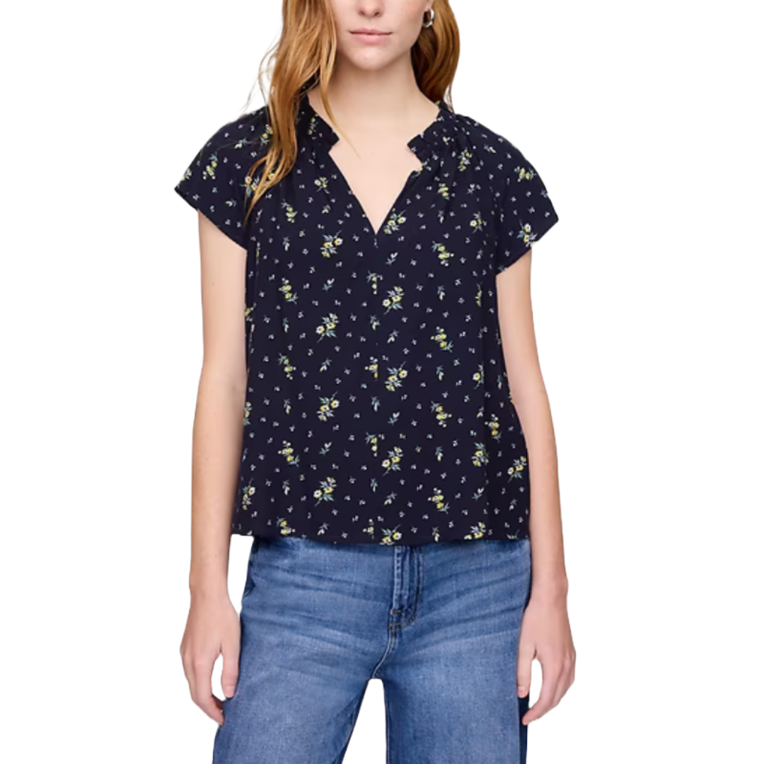 Navy blue splitneck top with short sleeves and a floral pattern in shades of green and light blue, paired with blue jeans.