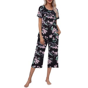 A woman is wearing a floral black pajama set with short sleeves and calf-length pants, featuring pink and green flower patterns.