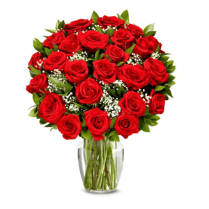 A bouquet of vibrant red roses with green leaves and small white flowers, arranged in a clear glass vase.