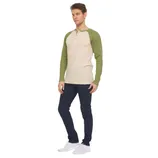 A man is wearing a cream and green long-sleeve henley shirt with dark blue jeans and white sneakers.