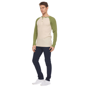 A man is wearing a cream and green long-sleeve henley shirt with dark blue jeans and white sneakers.
