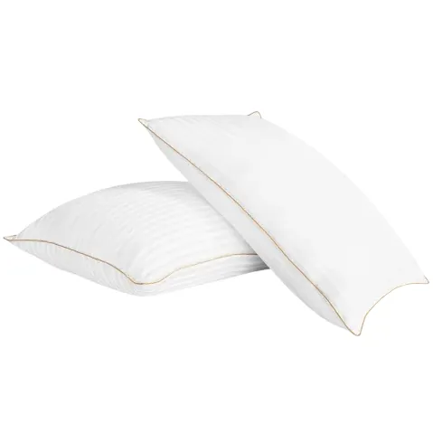 Two white pillows with subtle stripes and gold trim are stacked on top of each other.