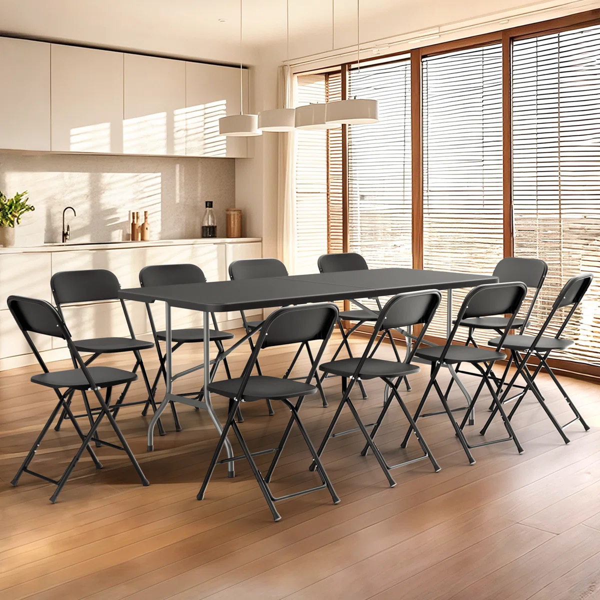 A kitchen with a wooden floor features a rectangular black table surrounded by eight black folding chairs. The space is bright, with large windows and white cabinetry.