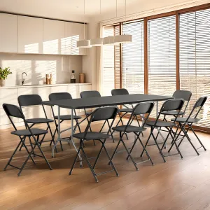 A kitchen with a wooden floor features a rectangular black table surrounded by eight black folding chairs. The space is bright, with large windows and white cabinetry.