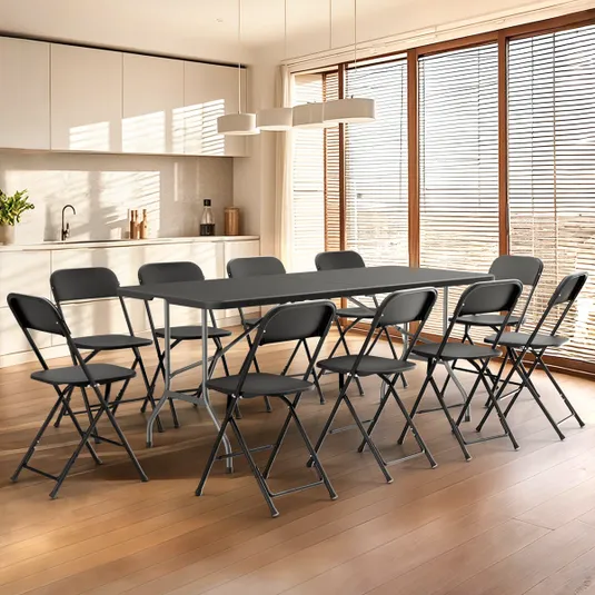A kitchen with a wooden floor features a rectangular black table surrounded by eight black folding chairs. The space is bright, with large windows and white cabinetry.