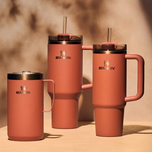 Three insulated drinking vessels with handles and lids by Stanley in varying sizes; two tall with straws, one shorter without.