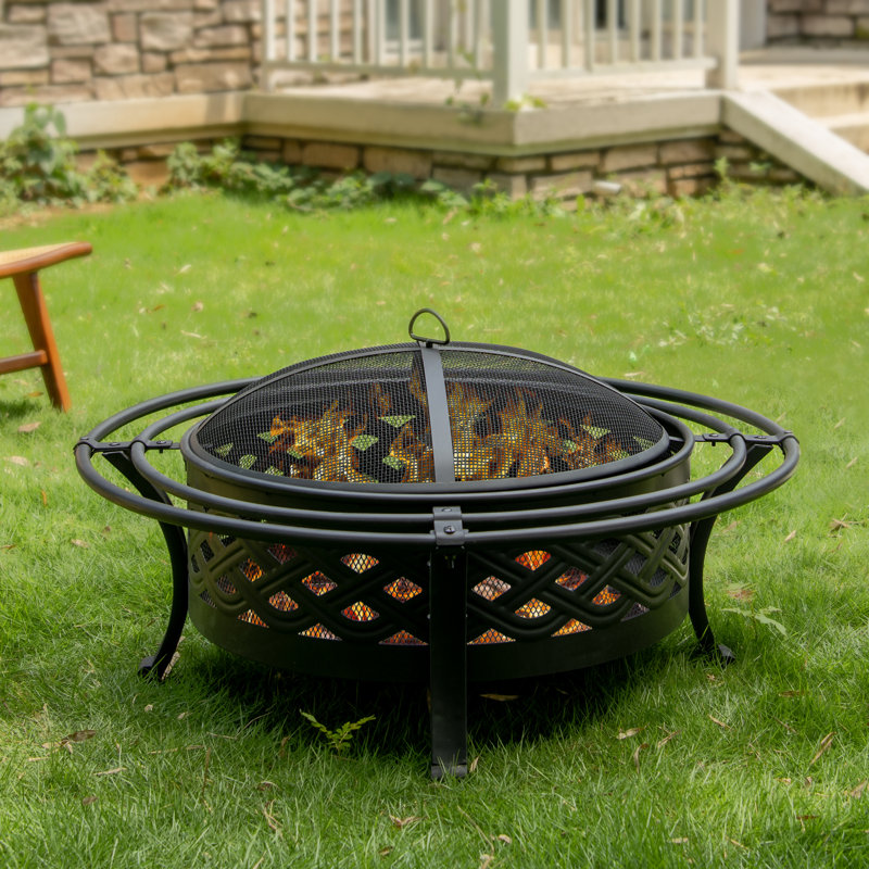 A round, metal fire pit with a mesh cover is set on a grassy lawn.