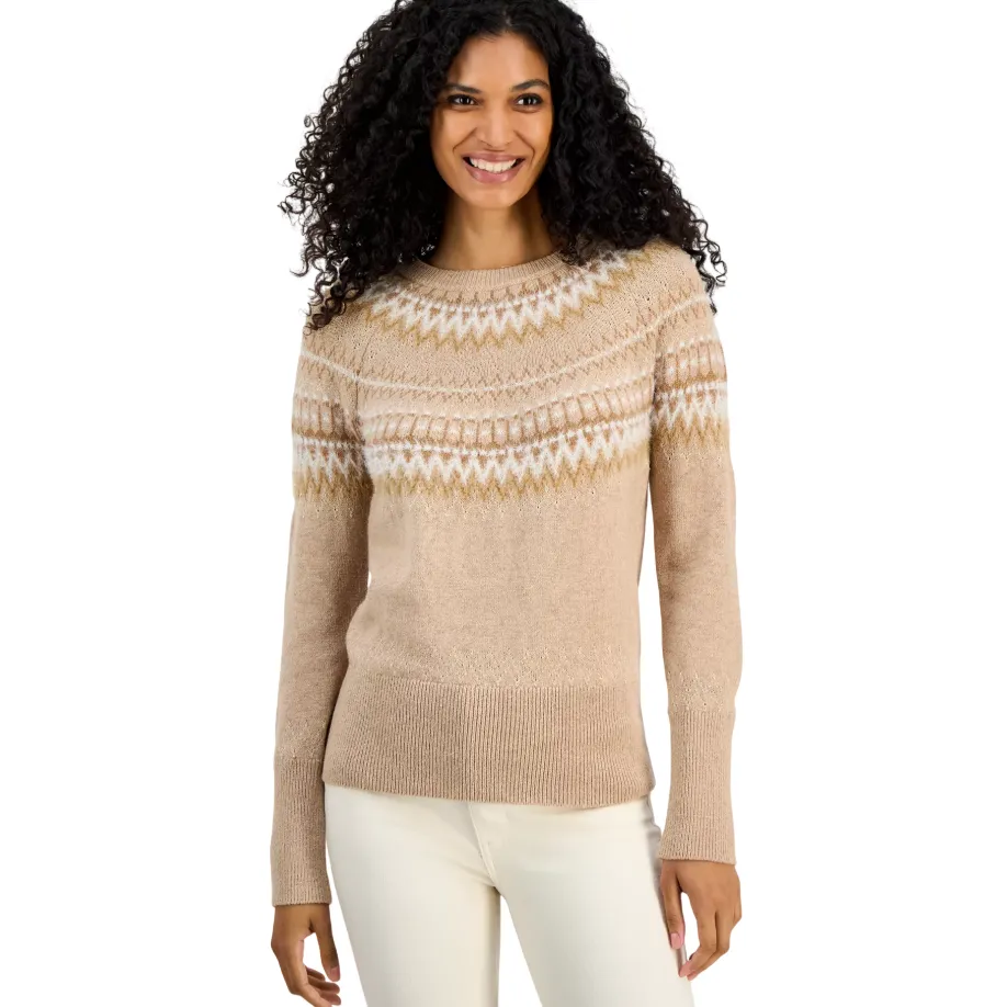 A woman is wearing a beige sweater with a Fair Isle pattern across the chest and shoulders, paired with off-white pants. The sweater features a ribbed neckline, cuffs, and hem.