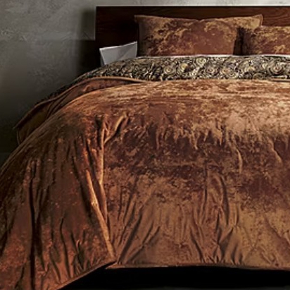 A luxurious brown velvet bedding set featuring a comforter, pillows, and a patterned throw. The texture appears plush and rich, adding a touch of elegance to the bedroom decor.