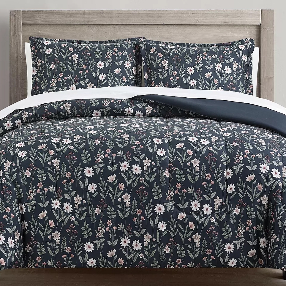 Floral-patterned bedding set with a navy blue background, featuring white and pink flowers, displayed on a wooden headboard bed.