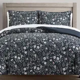 Floral-patterned bedding set with a navy blue background, featuring white and pink flowers, displayed on a wooden headboard bed.