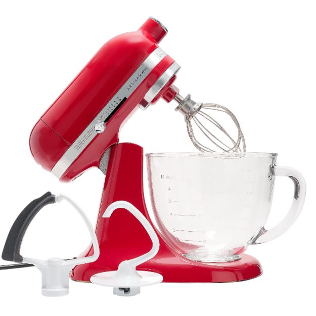 Red stand mixer with a glass bowl, featuring a whisk attachment installed. Also shown are a paddle and a dough hook attachment.