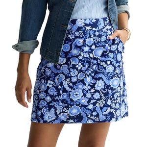 A woman wears a blue floral skirt paired with a light blue ribbed top and a denim jacket with rolled-up sleeves.
