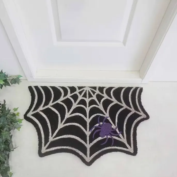 A spider web-shaped doormat with a purple spider design on it, placed on the floor by a door.