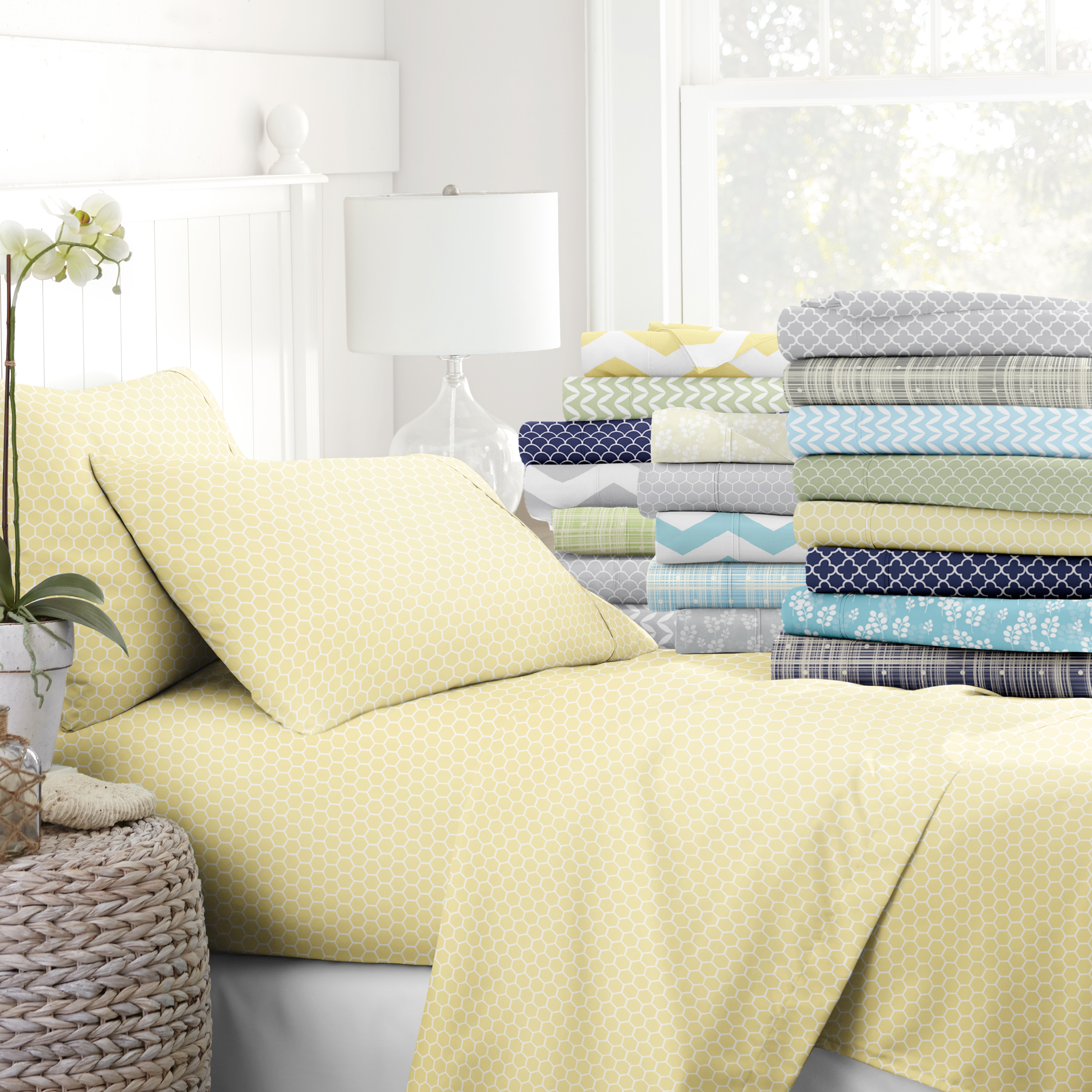 Various patterned bed sheet sets are displayed on a bed and stacked, including a prominently featured yellow geometric design.