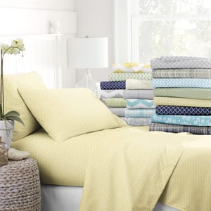 Various patterned bed sheet sets are displayed on a bed and stacked, including a prominently featured yellow geometric design.