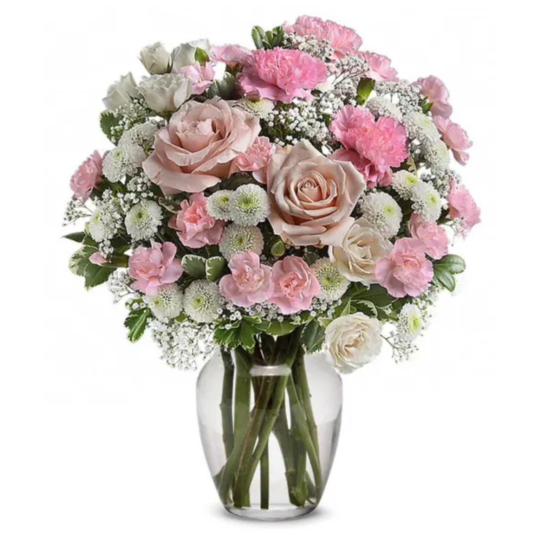 A floral arrangement in a glass vase featuring pink roses, pink carnations, white chrysanthemums, and baby's breath, complemented by green foliage.
