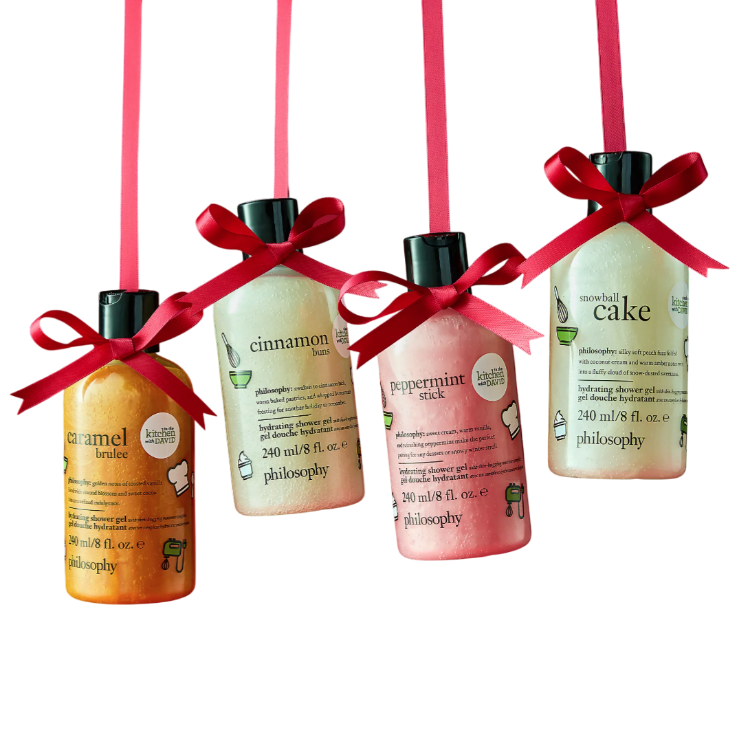 Four Philosophy bath products with silky finishes and festive scents: Caramel Brulee, Cinnamon Buns, Peppermint Stick, and Snowball Cake, each 240 ml, are creatively hung with red ribbons against a red background.