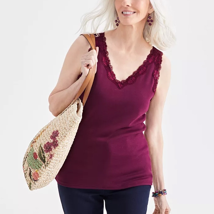 A woman wearing a burgundy sleeveless top with lace trim, carrying a straw tote bag with floral embroidery.