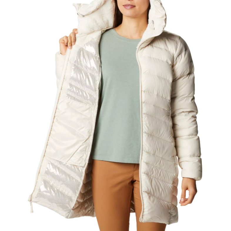 A woman wearing a beige puffer coat with a hood and a light green top paired with brown pants.