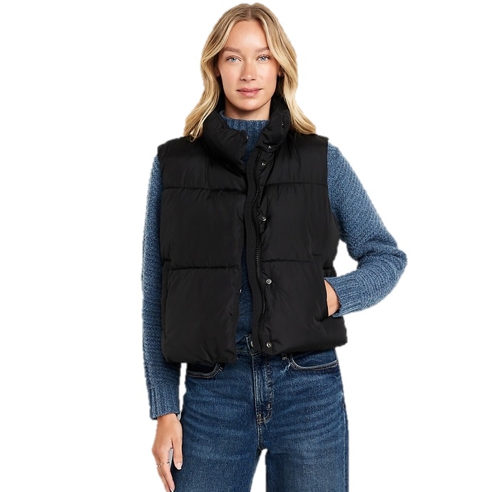 A woman wearing a black puffer vest over a blue sweater, paired with jeans.