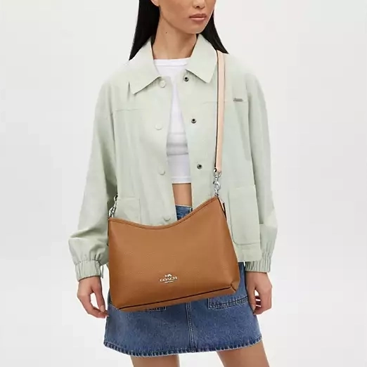 A woman wearing a pastel green jacket, white top, denim skirt, and holding a tan shoulder bag.