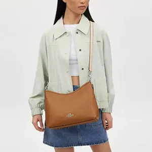 A woman wearing a pastel green jacket, white top, denim skirt, and holding a tan shoulder bag.