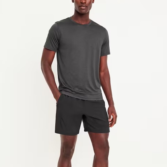 A man is wearing a dark gray, crew neck t-shirt paired with black athletic shorts that reach mid-thigh.