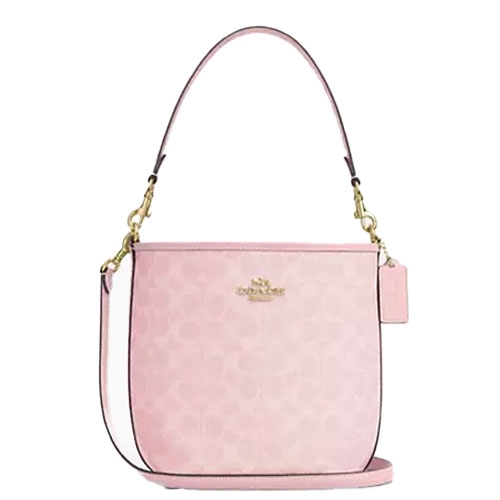 A light pink Coach bucket bag featuring a subtle monogram pattern, gold-tone hardware, a short top handle, an adjustable shoulder strap, and a hanging tag accent.