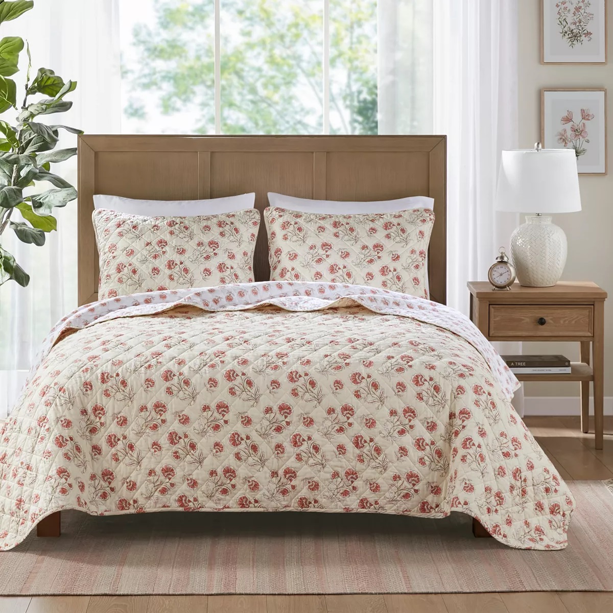A reversible quilt set featuring a beige background with red floral patterns, including two matching pillow shams with the same design. The bedding is displayed on a bed in a room with neutral decor.
