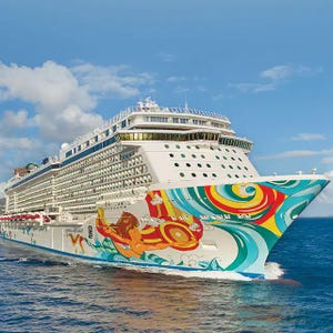 A large cruise ship with a colorful, abstract design on its hull sails on the ocean.