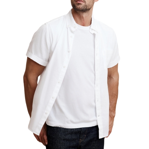 White short-sleeve Oxford shirt worn over a plain white t-shirt, paired with dark pants. The shirt has a button-down front and a crisp, casual style.