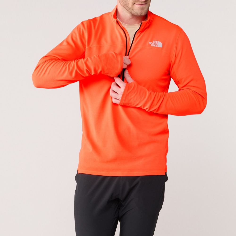 A man wearing a bright orange long-sleeved athletic shirt with a half-zip front and black pants.
