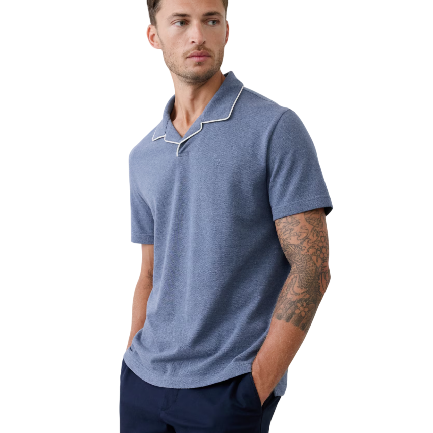 A man is wearing a short-sleeve blue polo shirt with white piping on the collar, paired with dark navy pants.