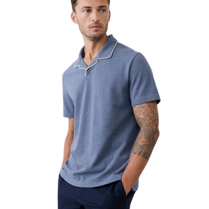 A man is wearing a short-sleeve blue polo shirt with white piping on the collar, paired with dark navy pants.