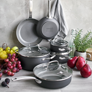 A 10-piece GreenPan cookware set, featuring a ceramic non-stick coating, includes various sizes of pots and pans with glass lids and stainless-steel handles, alongside fresh fruit and herbs.