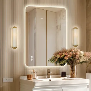 A bathroom scene featuring a backlit rectangular mirror with touch controls, modern wall sconces, a white sink, and a vase of flowers.