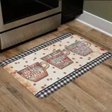 Kitchen floor mat with a coffee theme, featuring three cups adorned with coffee-related words, surrounded by coffee bean motifs and bordered with a black and white checkered pattern.