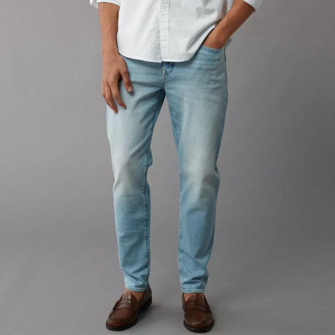 Light blue men's jeans with a slim fit design, paired with brown loafers and partially tucked-in white shirt.