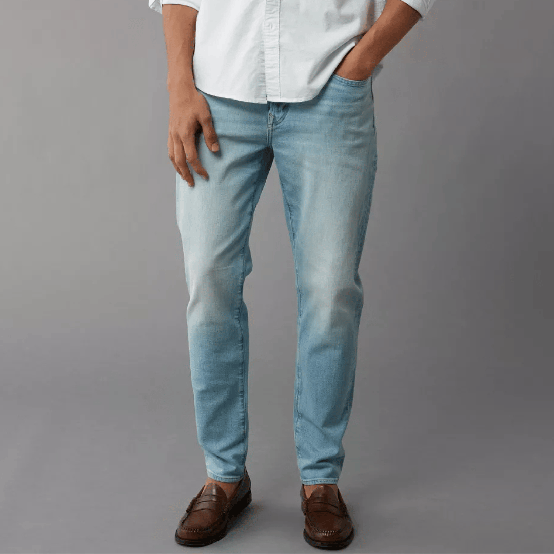Light blue men's jeans with a slim fit design, paired with brown loafers and partially tucked-in white shirt.