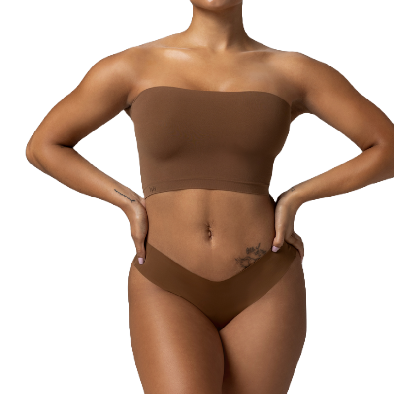 A woman is wearing a brown strapless bandeau top and matching underwear, with visible tattoos on her hip and wrist.
