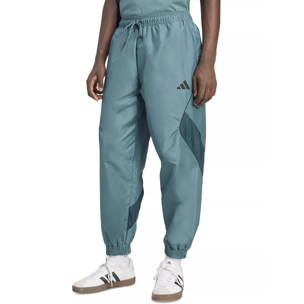 A person is wearing teal track pants with a small logo on the thigh, paired with white sneakers featuring black stripes and gum soles.