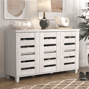 A wooden sideboard with slatted doors, featuring a light finish. It holds decorative items, including a lamp, a shell ornament, and a vase.