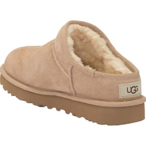 A beige UGG slip-on shoe with shearling lining and a brown rubber sole, featuring the UGG logo on the heel.