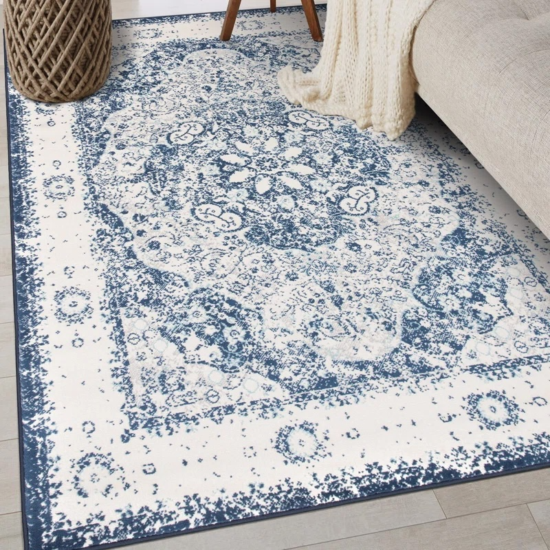 A blue and white patterned area rug is placed on a light wooden floor next to a beige sofa and a woven basket.