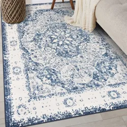 A blue and white patterned area rug is placed on a light wooden floor next to a beige sofa and a woven basket.