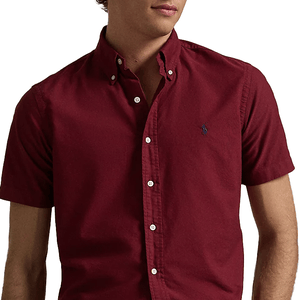A short-sleeve, button-down maroon shirt with a small embroidered blue logo on the chest, featuring classic buttoned collar.